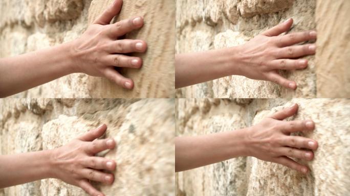 女人的手在古老的石墙上移动。