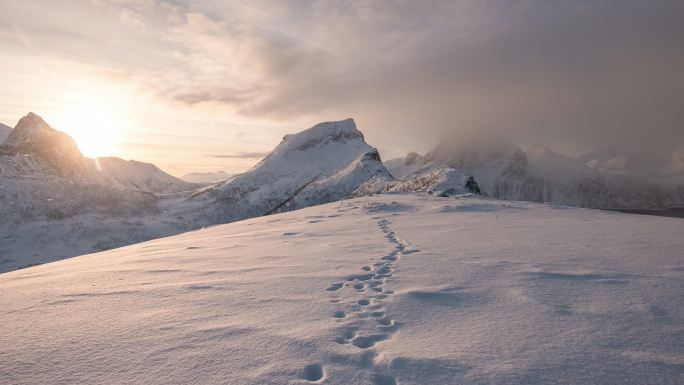 雪山山脉的时间推移与日出时雪地上的脚印