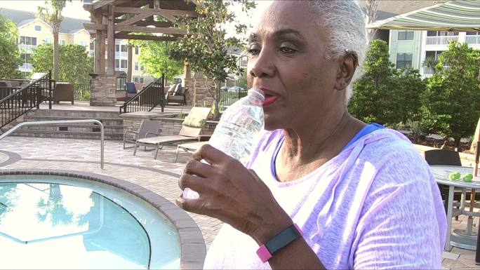 一位老妇人在游泳池边喝着一瓶水