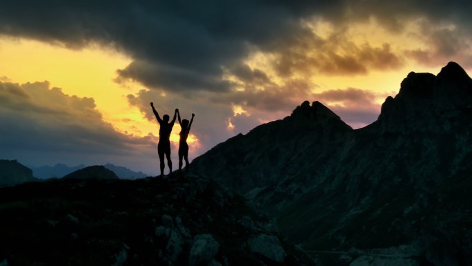 两名徒步旅行者举起双手站在山顶上的剪影