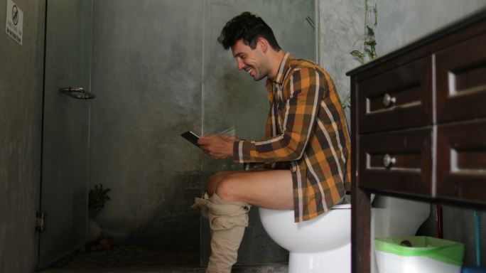 坐在马桶上使用手机在网上聊天的年轻人