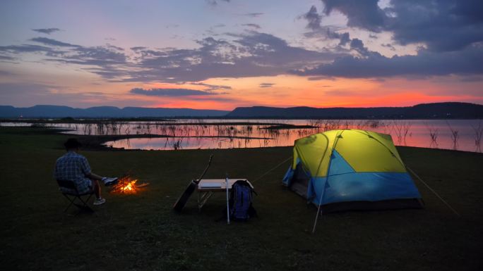 老人坐在帐篷旁，在湖边享受篝火风景
