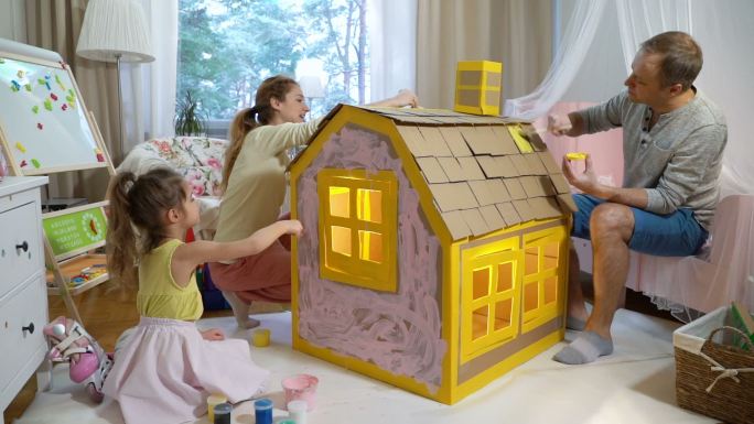 父母陪女儿一起建造和粉刷玩具纸板房子