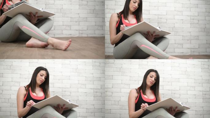年轻的孕妇坐在地板上在看相册