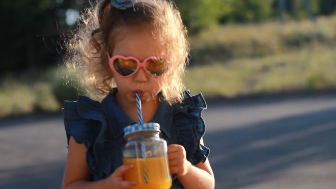 夏日，戴墨镜的小女孩在夕阳下喝着果汁