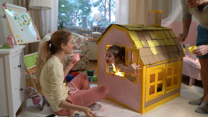 父母和孩子一起建造和粉刷玩具纸板房子