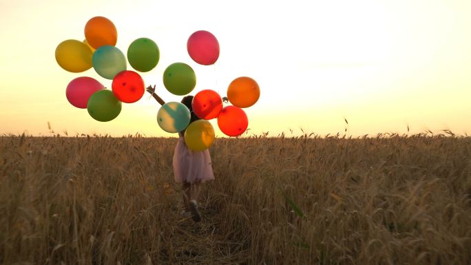 着五颜六色气球的年轻女孩正穿过田野。