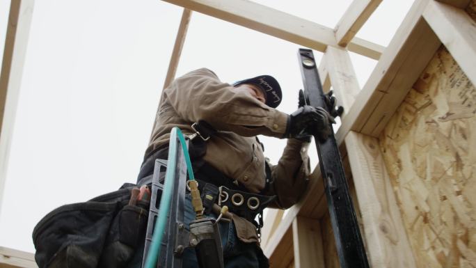 一名男子站在建筑框架上，用水平仪测量墙壁