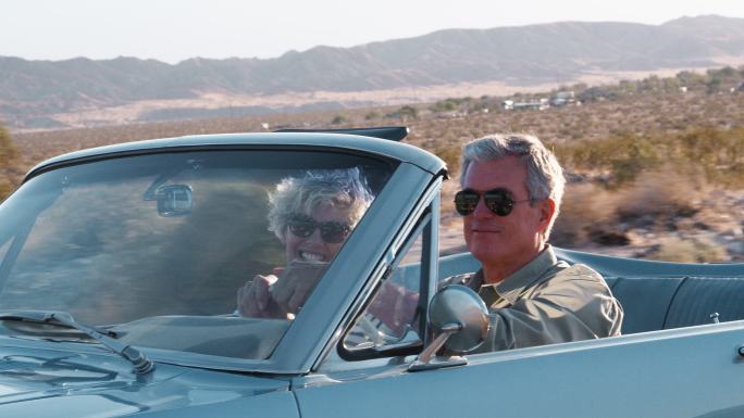 老年夫妇开着敞篷车在沙漠公路上行驶