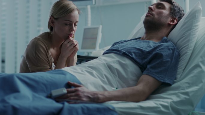 在医院里，病人躺在床上，妻子在祈祷。