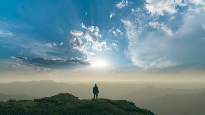 那人站在一座山上，背景是灿烂的阳光