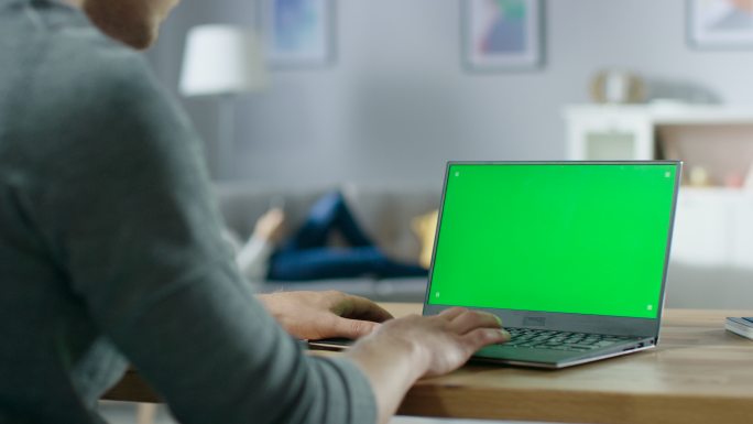 男人在带有绿色模拟屏幕的笔记本电脑上打字