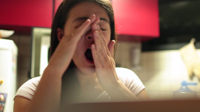 疲惫的女人在电脑屏幕前手捂着嘴打哈欠