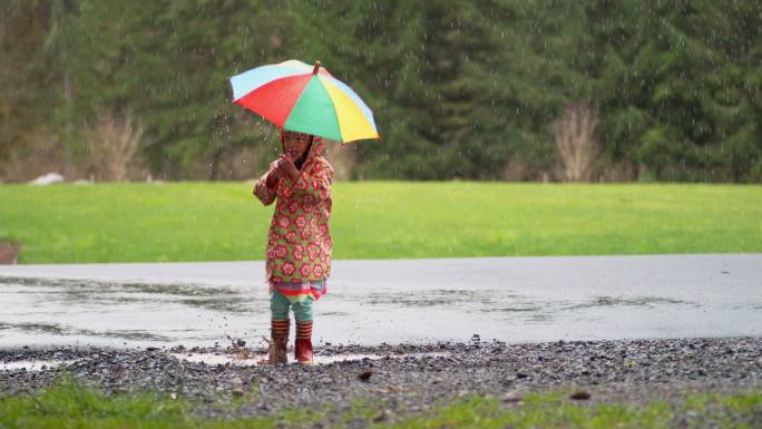 带着雨伞的小女孩在雨中嬉戏