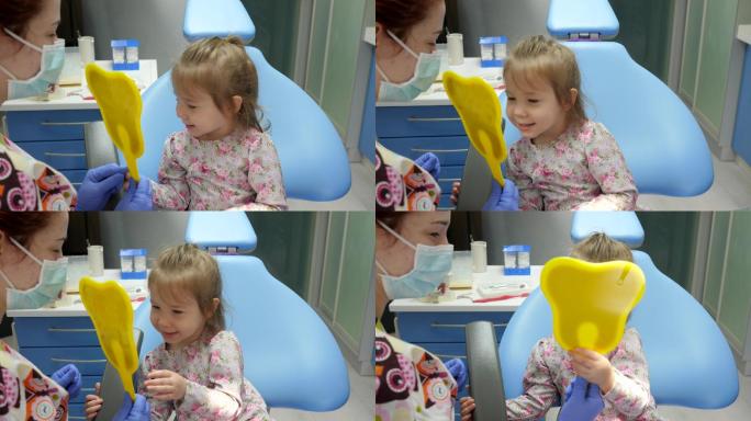 孩子坐在牙科椅上照镜子，牙医在旁边