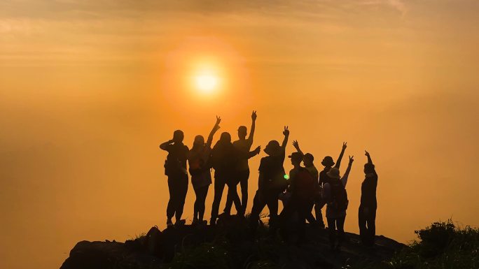 团队小伙伴们徒步登上山顶携手欢呼欣赏落日
