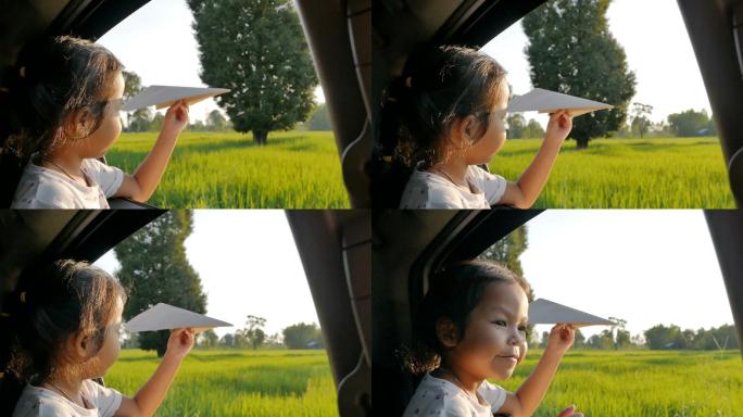 可爱的小女孩在车窗边玩纸飞机。