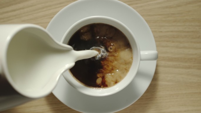 将牛奶从牛奶罐中倒入桌上的一杯黑咖啡