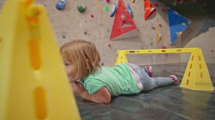 一个小女孩在攀岩馆的儿童栏下爬行