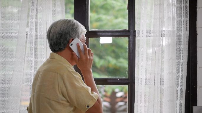 一位男士在家里靠窗边愉快地用智能手机交谈