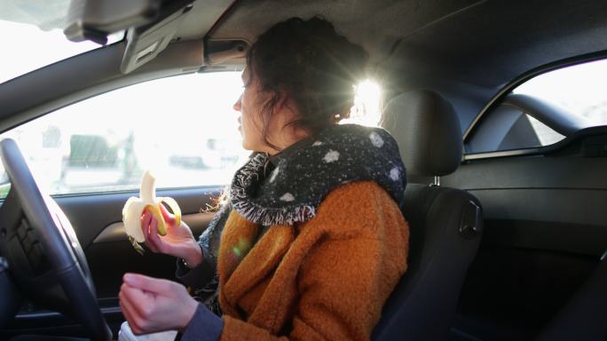 女人正坐在汽车的驾驶座上吃香蕉。