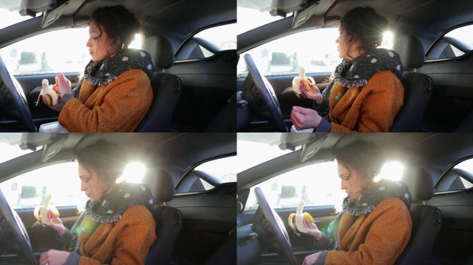 女人正坐在汽车的驾驶座上吃香蕉。