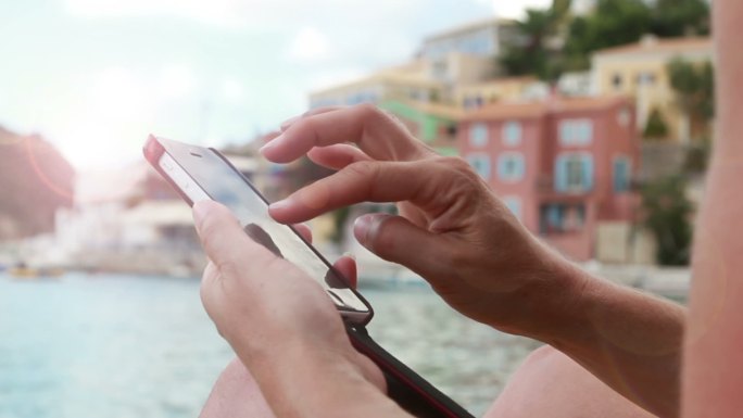 坐在希海滩上使用智能手机的近景照片