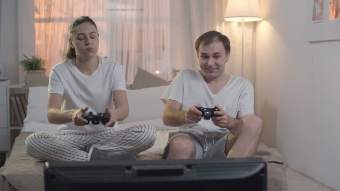 年轻夫妇坐在床上玩电子游戏，男人赢了