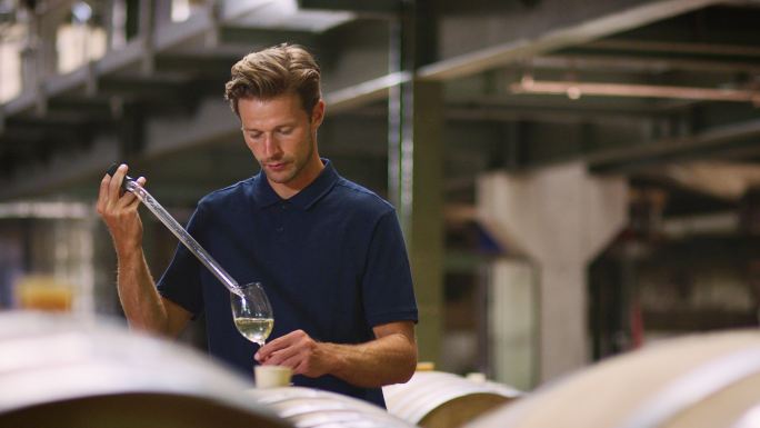 一个年轻人在一家葡萄酒厂的仓库里测试葡萄酒