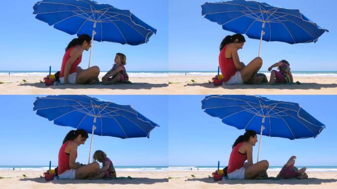 母亲和孩子在海滩上的蓝色大伞下休息
