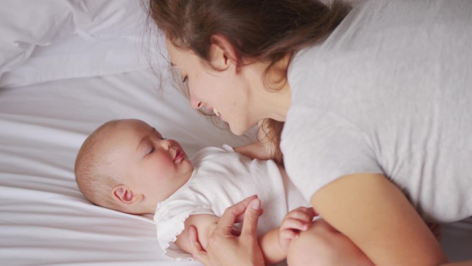 年轻妈妈抱着可爱的女婴躺在床上