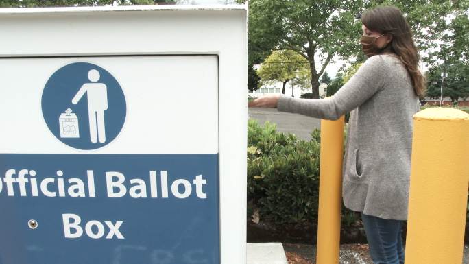 戴着口罩的妇女将选票投到选民的邮箱里