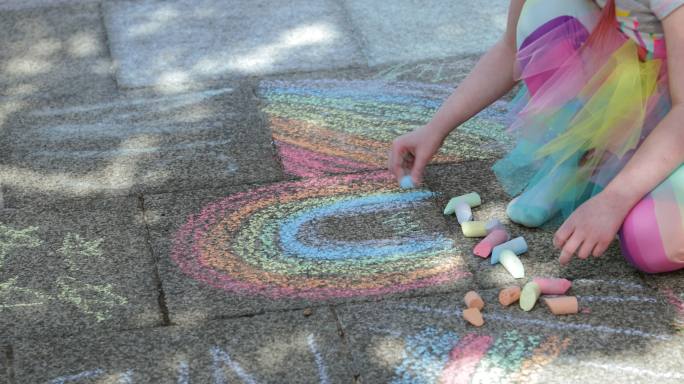 女孩坐在屋外的小路上用粉笔画彩虹