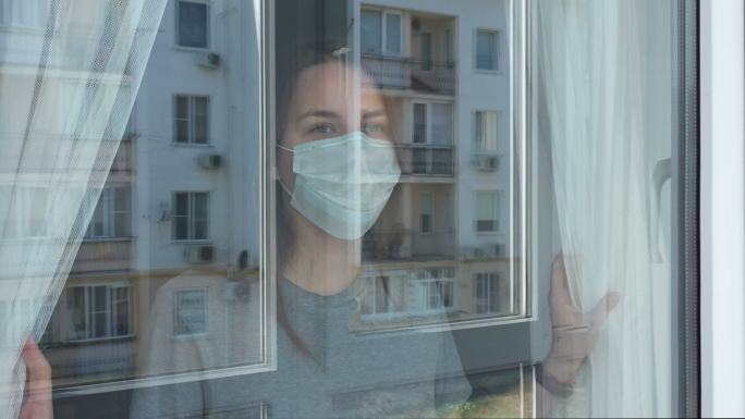 一名妇女望着窗外。留在家中自我隔离