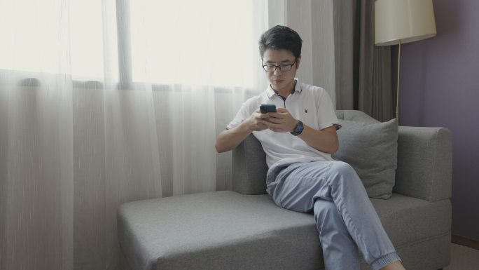 4K年轻男性在窗户旁边沙发上玩手机