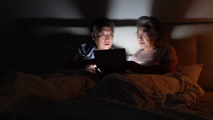 老年夫妇坐在床上使用平板电脑