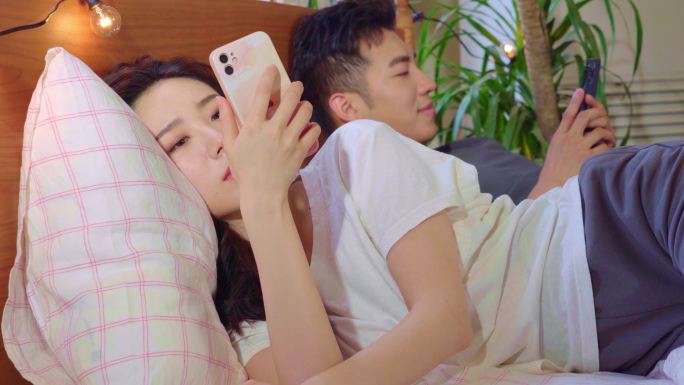 青年情侣躺在床上各自玩手机
