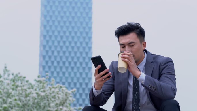 商务男士在户外喝咖啡看手机