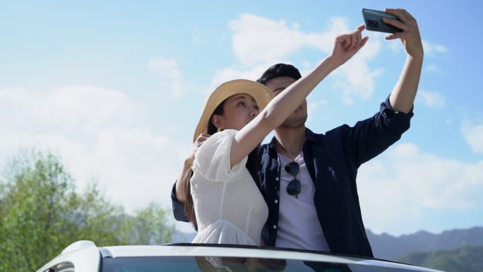 青年夫妻在汽车上用手机拍照