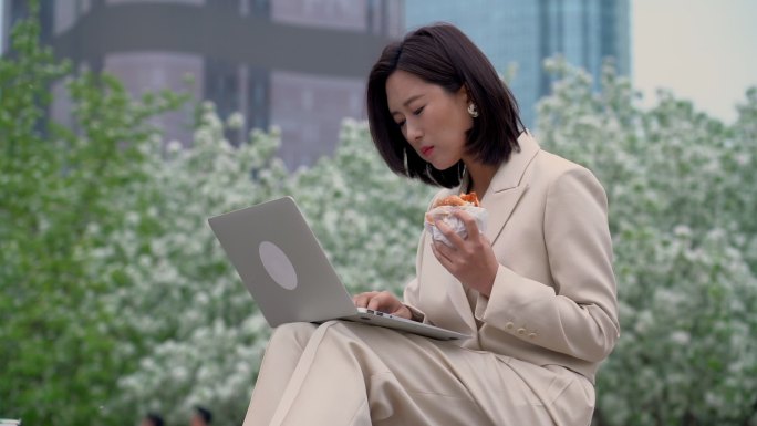 商务女性在户外边吃饭边用电脑