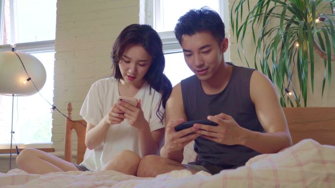 青年情侣坐在床上玩手机