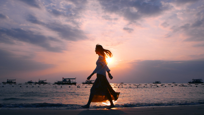 长发飘飘女生在夕阳下的海边漫步剪影