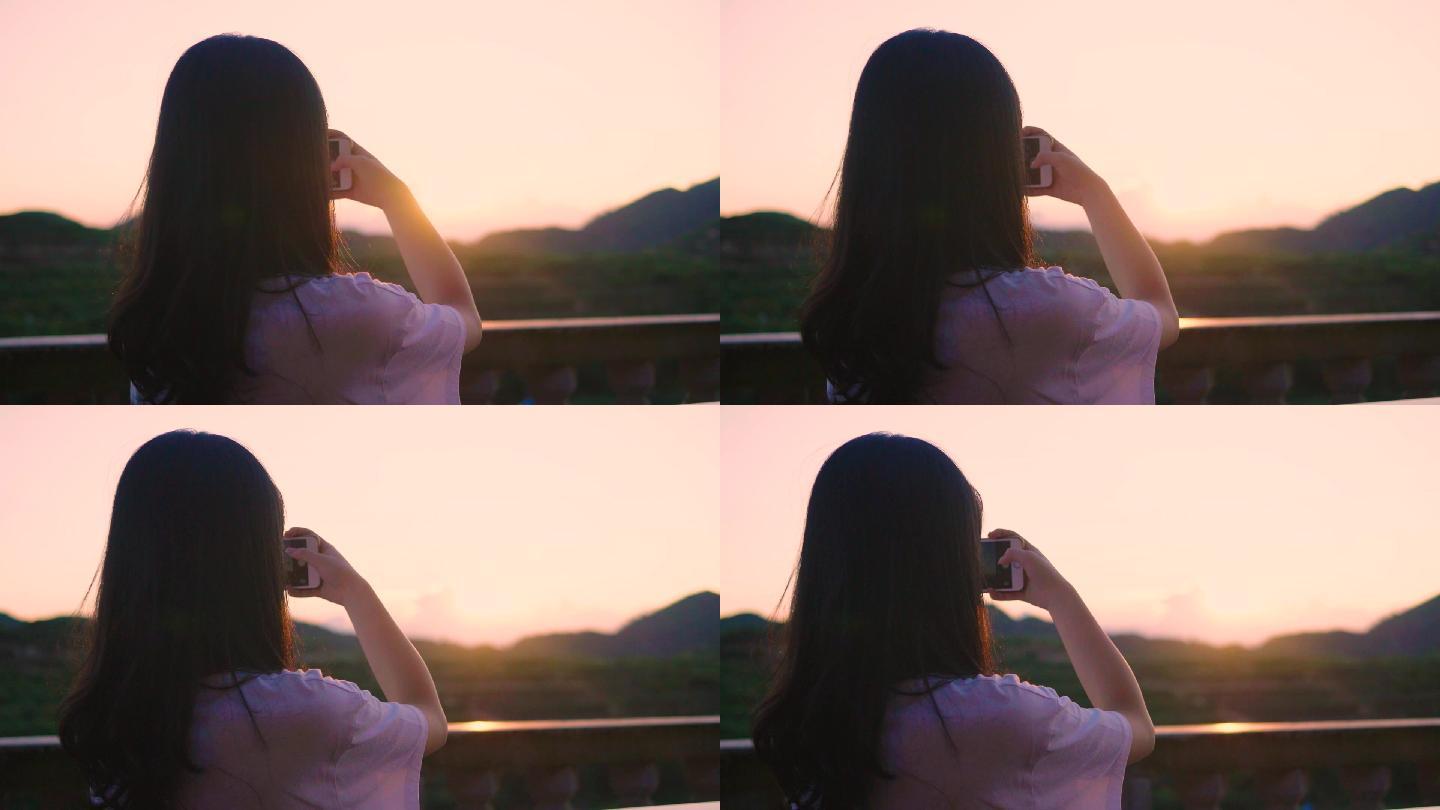 长发女孩拿手机拍摄美丽的夕阳逆光背影