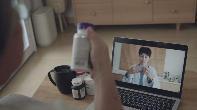 一名亚洲妇女在客厅里拿着药瓶，用笔记本电脑聊天。