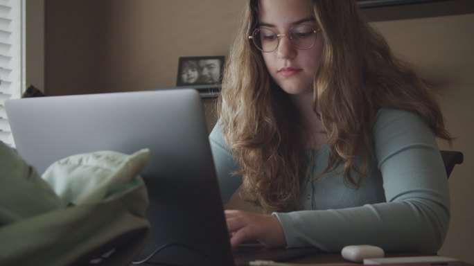 一个十几岁的女孩在家用笔记本电脑做功课