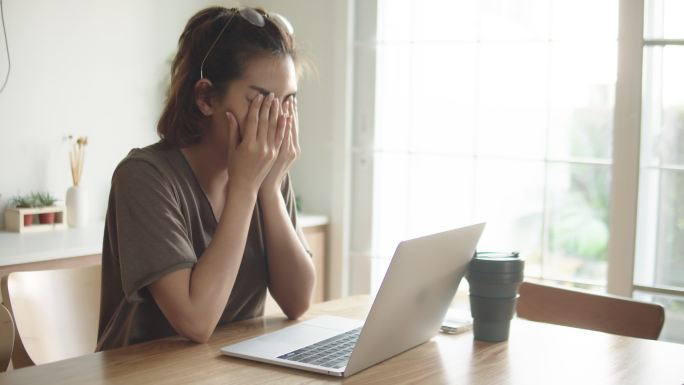 一名妇女在家里挣扎着使用笔记本电脑。