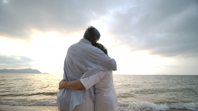 老年夫妇在海滩上相互拥抱。