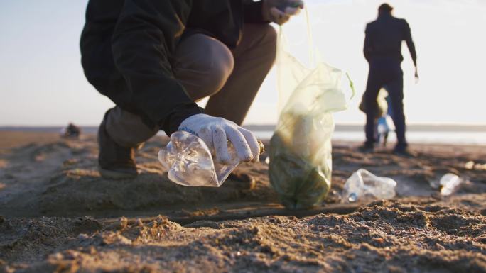 一个年轻人在海滩上捡起塑料瓶的特写镜头