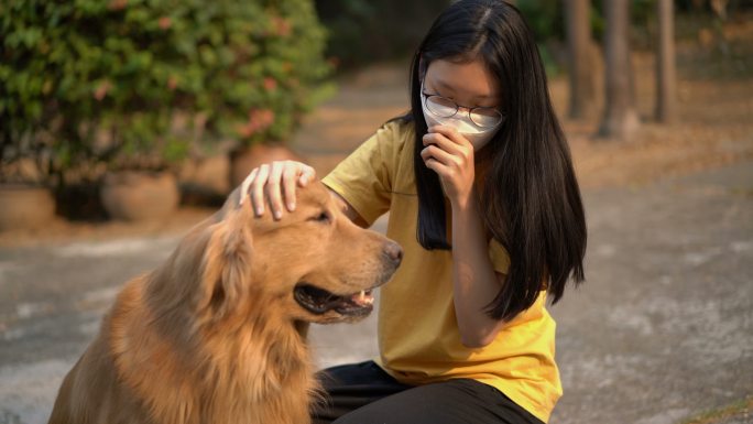 戴着口罩的少女拥抱金毛猎犬