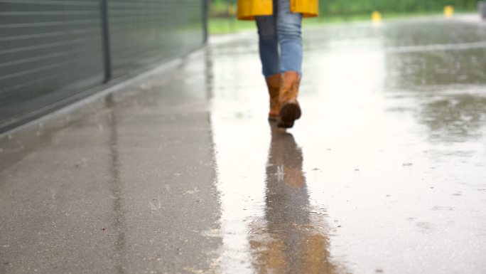 穿着黄色防水靴的脚在雨中走向摄像机。